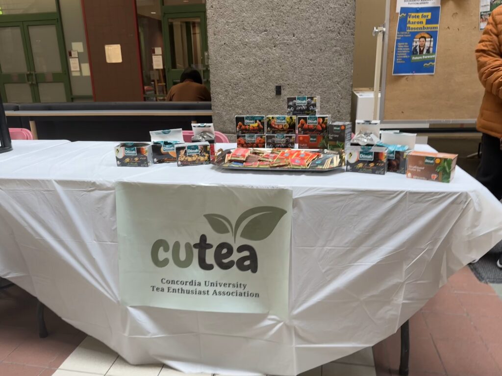 A table with a white tablecloth and a poster that says “CUTEA Concordia University Tea Enthusiast Association” has tea boxes and tea bags on display.